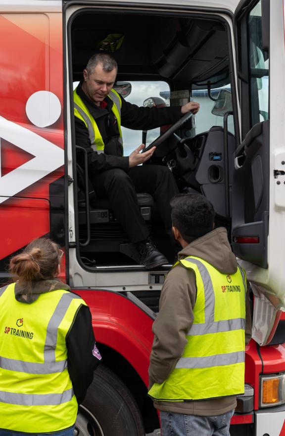 A learner speaking to two tutors from his cab in a truck