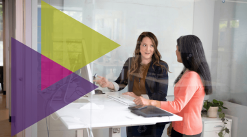 Two female colleagues chat at a stand up desk in a modern office